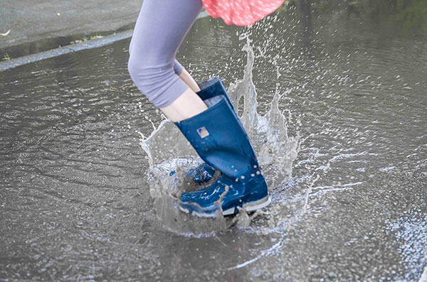 Een kind met laarzen springt in een plas in een overstroomde straat.