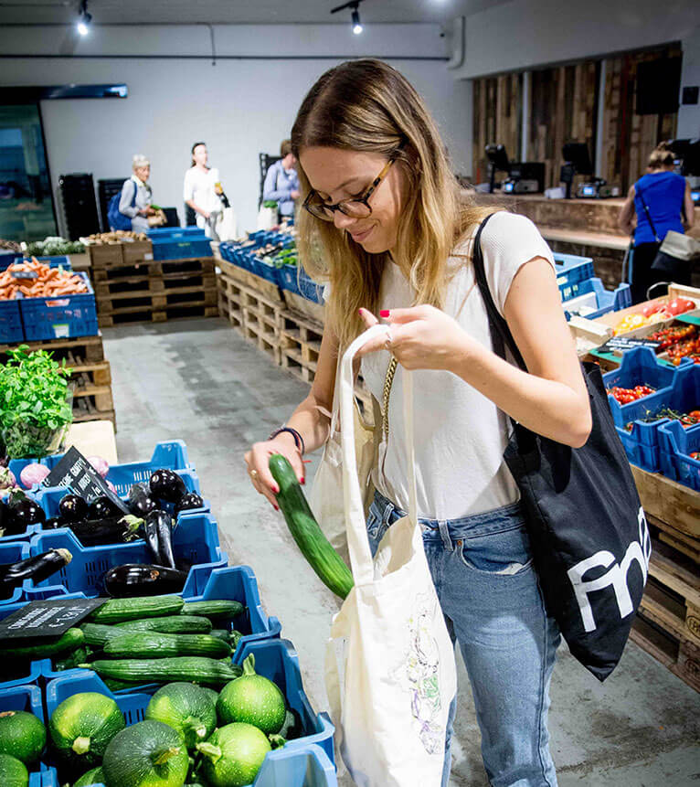 Een vrouw doet inkopen en steekt een komkommer in een stoffen zak