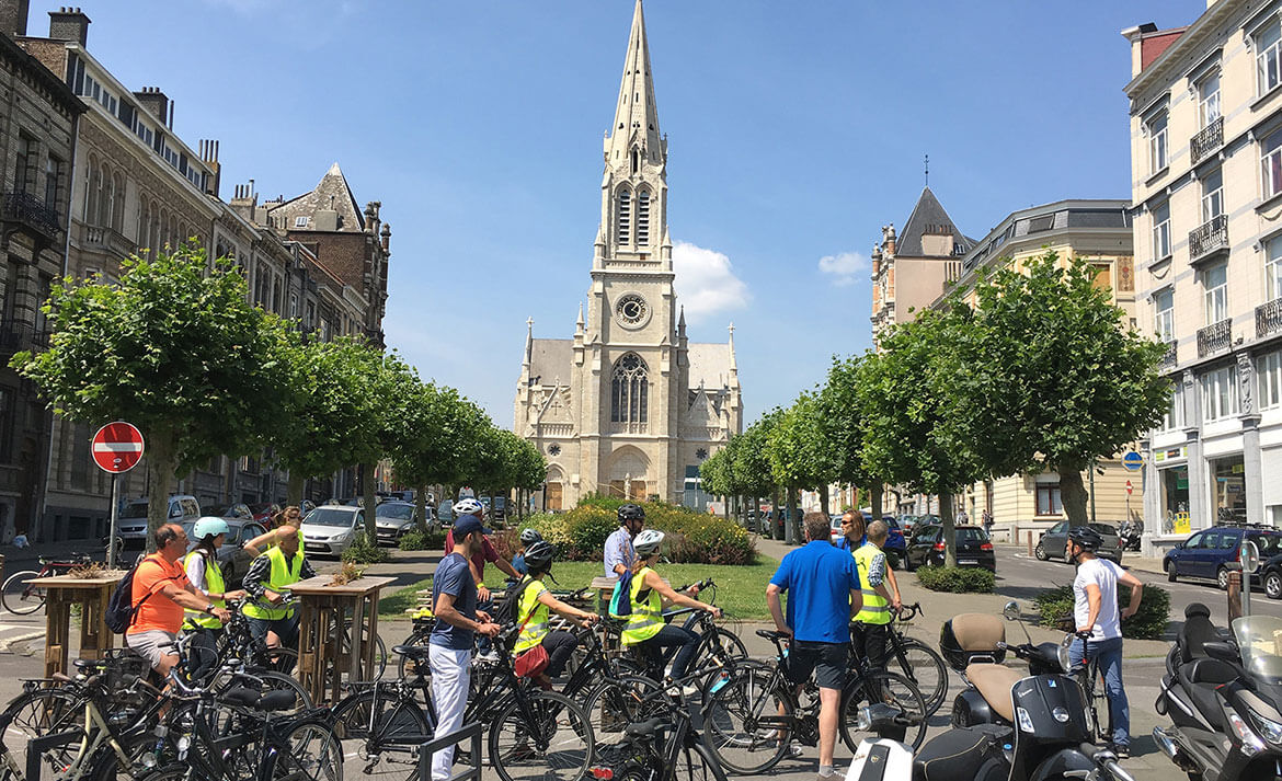 Een groep fietsers die stilstaat op een plein, met een kerk in de achtergrond