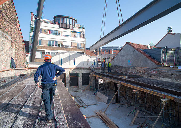 Een man op een dak met een veiligheidshelm houdt toezicht op de constructiewerkzaamheden van een gebouw