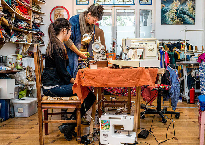 Twee vrouwen aan een tafel met een naaimachine en naaispullen in een naaiatelier
