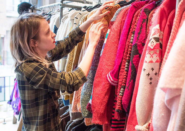 Een vrouw zoekt een kledingstuk in een tweedehandswinkel