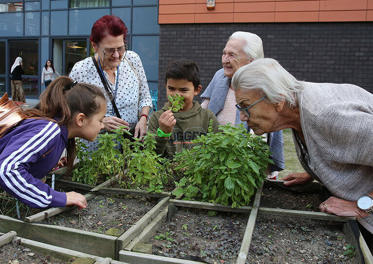 Drie oudere mensen en twee kinderen die ruiken aan de planten van een moestuinbak in een rusthuis
