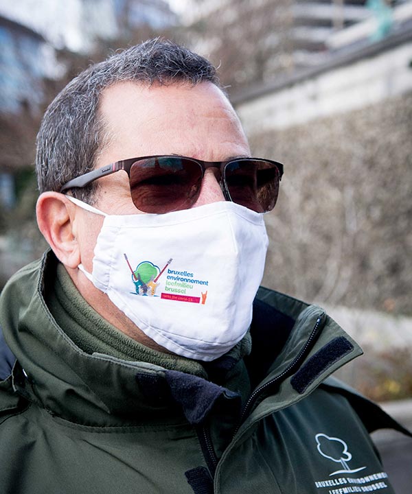 Een parkwachter draagt een mondmasker met het logo van Leefmilieu Brussel. 